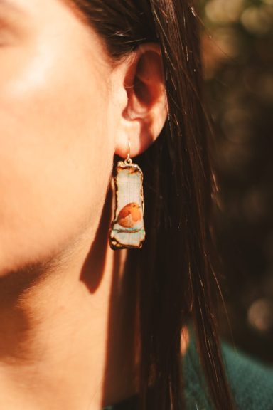 Pendientes rectangulares con una ilustración de un pájaro en un fondo claro.