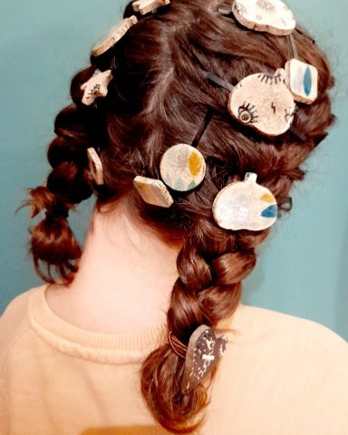 Chica con trenzas y adornos coloridos en el cabello, visto desde atrás.